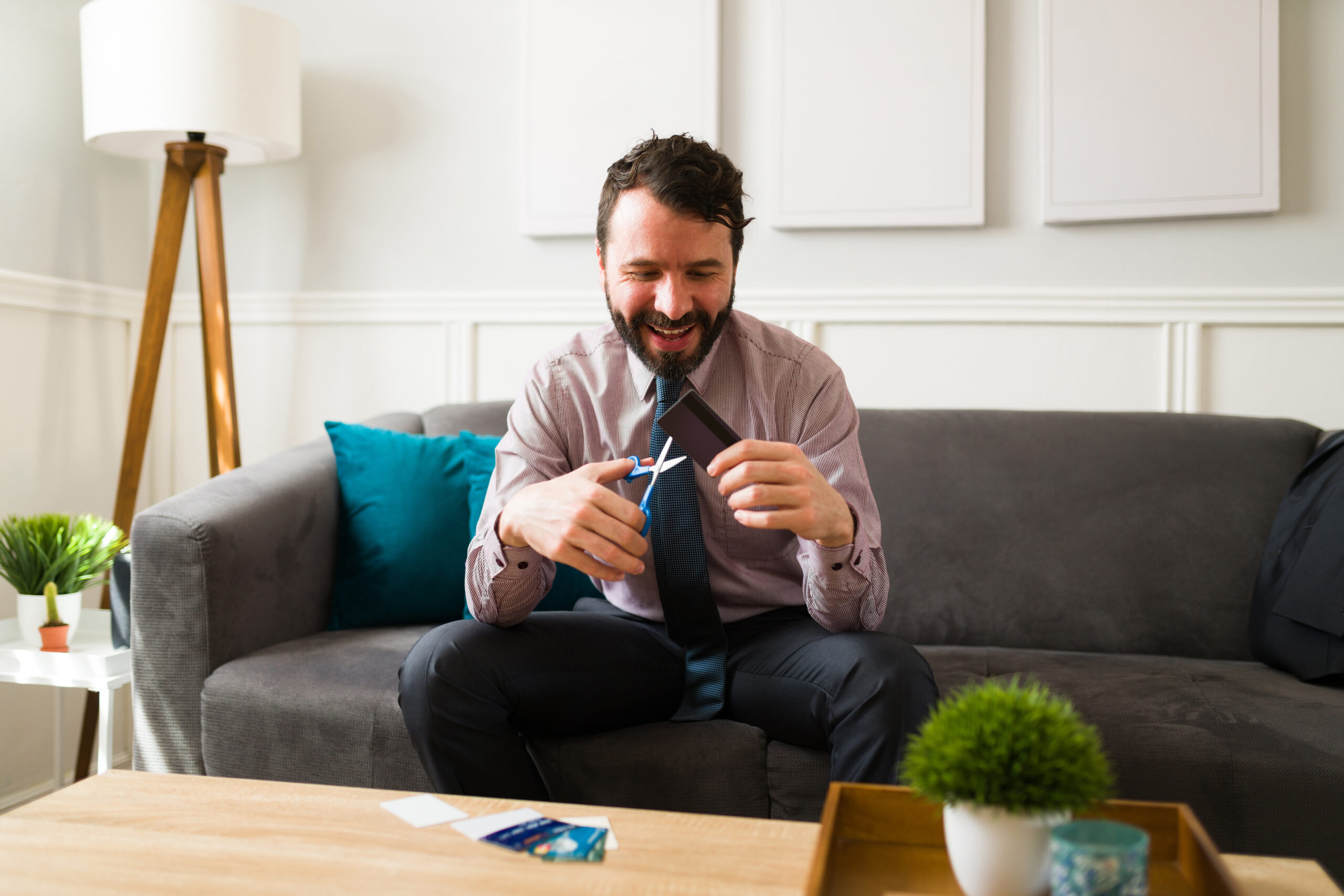 Man sites on couch, cutting up his credit cards, enjoying debt-free life. It's the kind of life that only comes with careful financial planning.